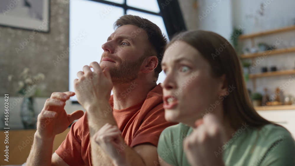 Worried spouses cheering football game at TV sitting couch dissatisfied closeup.