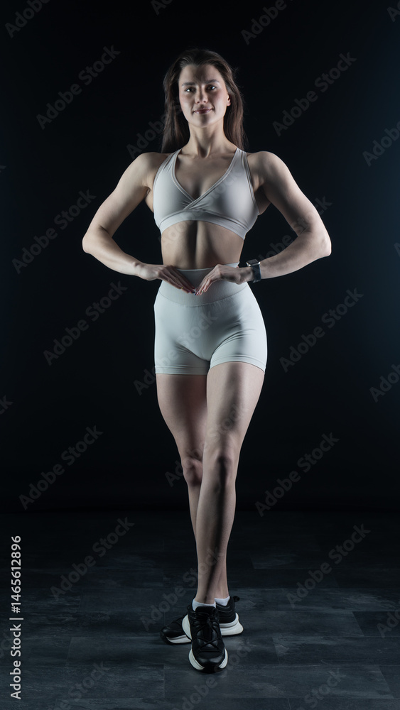 Obraz premium Young beautiful woman with athletic body on dark background. Fitness girl