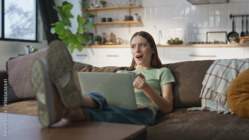 Home girl videocalling laptop lying comfortable apartment sofa with coffee cup.