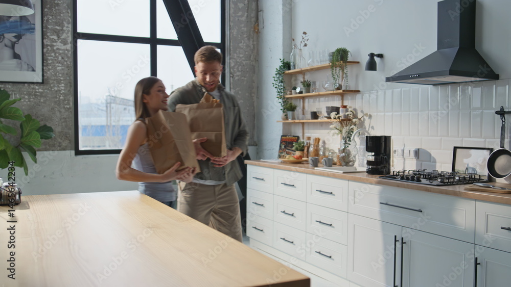 Obraz premium Smiling spouses bringing groceries to home kitchen closeup. Cheerful family