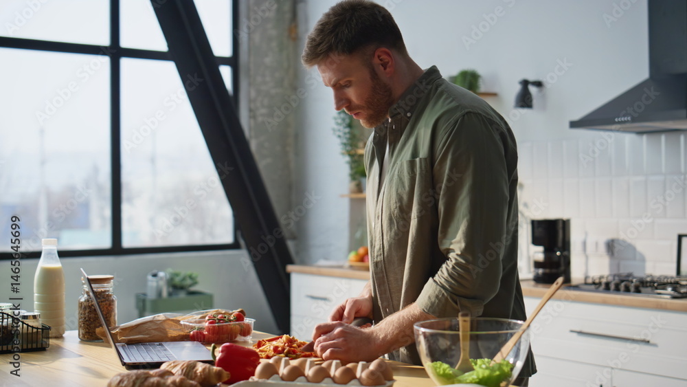 Man watching laptop recipe chopping vegetables in kitchen countertop closeup.