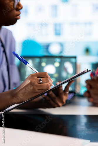 Obraz na płótnie African american nurse takes notes during consultation with old people, creating the healthcare records with symptoms and other problems. Ensuring an easy recovery plan, clinical setting. Close up. w salonie