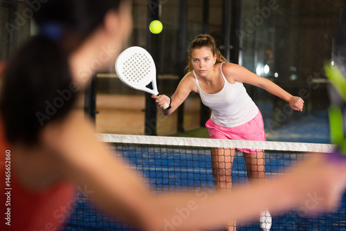 Young beautiful woman in white t-shirt playing padel tennis indoor