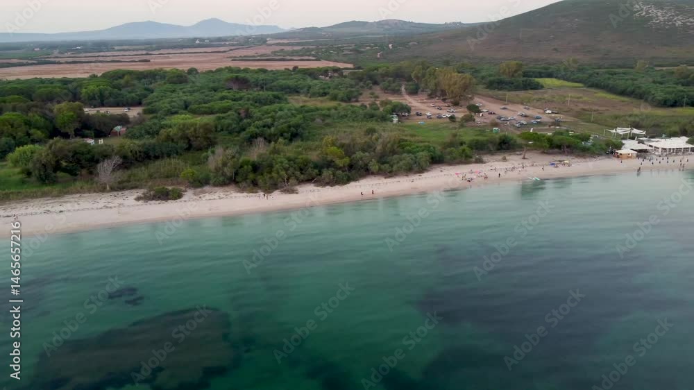 Aerial view of Mugoni beach near Alghero in Sardinia island, with people sunbathing, a beach bar and some boats anchored in calm sea Aerial view of Mugoni beach near Alghero in Sardinia island, with people sunbathing, a beach bar and some boats anchored in calm sea