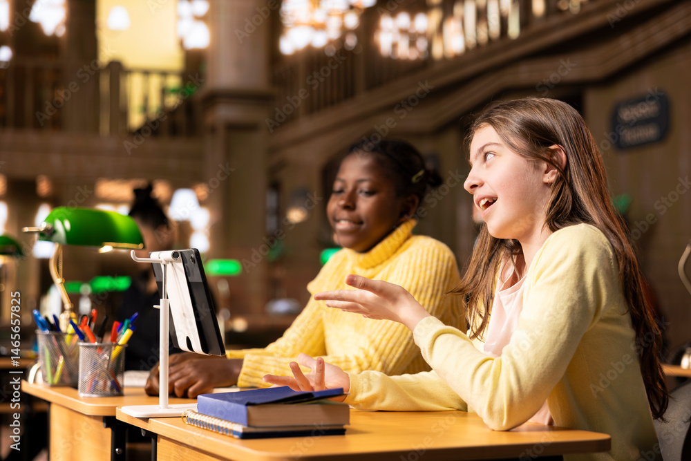Girls participating in an online course at the library joining a live video webinar with their teacher to complete a school project. Scholars working on an assignment via video call lesson.