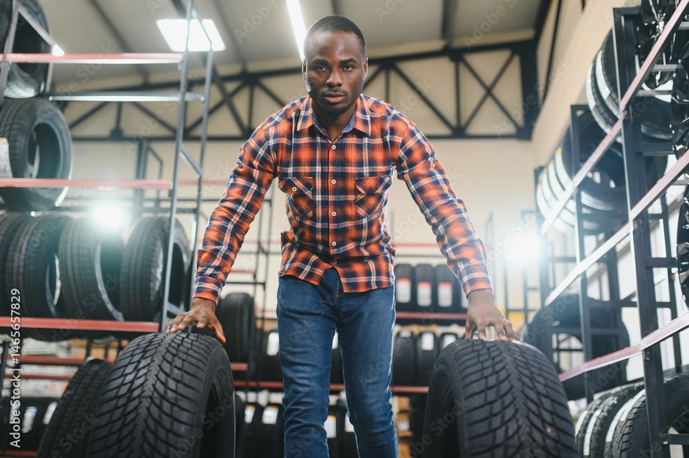 Fototapeta premium Male studying car tire in market. African american guy in casual wear stand looking at tire, make choice. shopping time