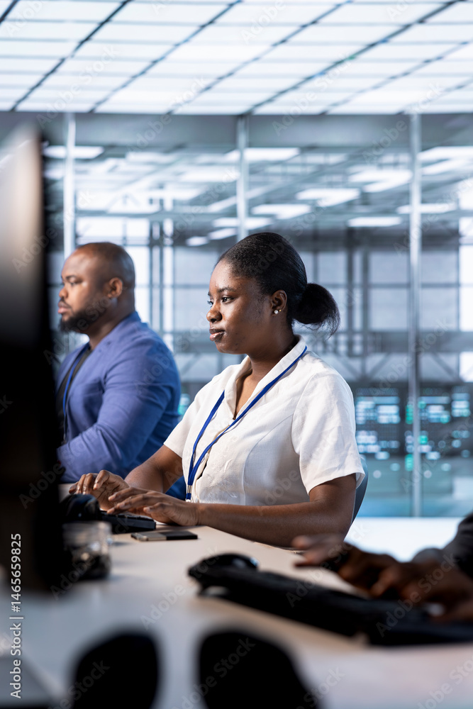 African american admin in data center using PC to check for server performance issues arising due to high CPU usage. Woman in server hub fixing insufficient memory errors slowing down hardware