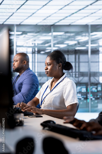 African american admin in data center using PC to check for server performance issues arising due to high CPU usage. Woman in server hub fixing insufficient memory errors slowing down hardware
