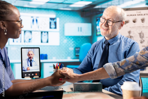 Obraz na płótnie African american nurse doing comforting gesture for senior people on web call with specialist, holding hands with patients and encouraging them while they discuss with doctor remotely. Telemedicine. w salonie