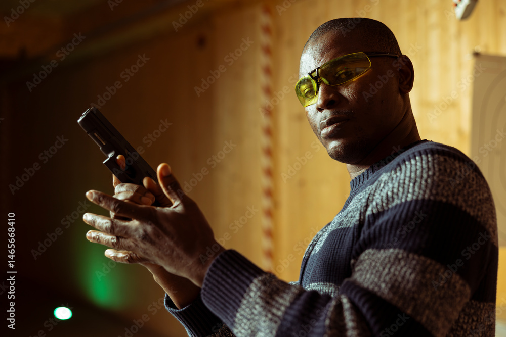 Portrait of man in indoor shooting range offering rental firearm for tryouts, doing training. African american novice in firing range facility getting hands on experience with handgun