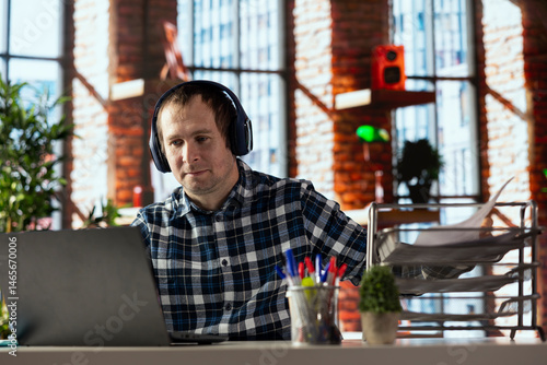 home office worker at desk using laptop, engaging in video call, participating in virtual meeting with colleagues. Man discussing with coworkers during videoconference meeting, using headset