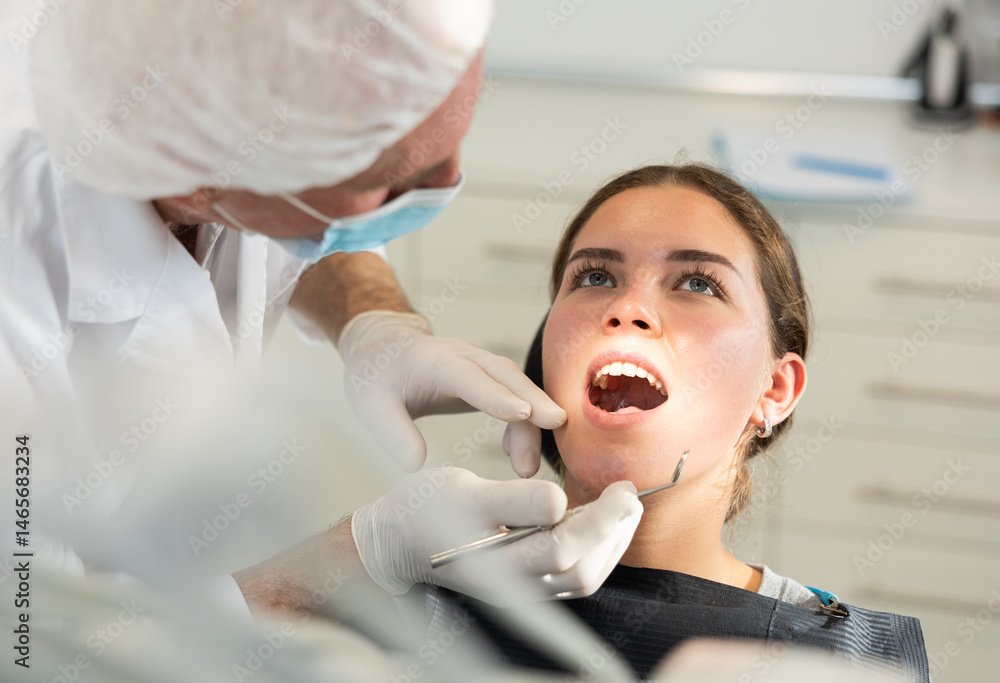 Mature man dentist examines teeth of young female patient before treatment in dental clinic