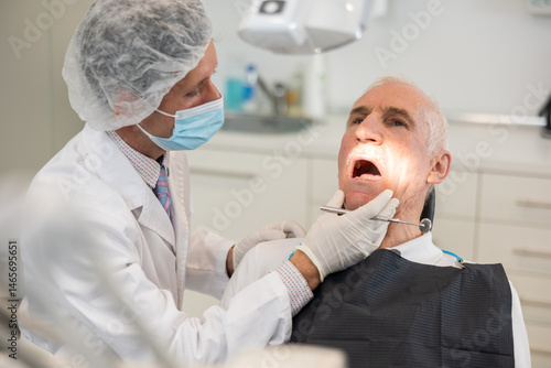 Adult male doctor dentist examining teeth of elderly male patient before treatment in office
