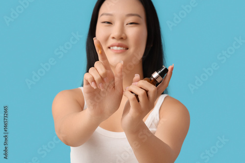 Young Asian woman with bottle of oil on blue background, closeup