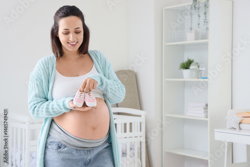 Young pregnant woman with baby booties in children's bedroom