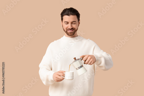 Young man with geyser coffee maker and cup on beige background