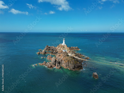 Scenic aerial drone view of La Corbiere lighthouse on a rocky island surrounded by turquoise water. Jersey, Channel Islands