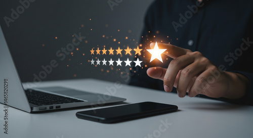 Person giving a five star rating with a laptop and phone on a desk in a dimly lit environment real estate business ,technology ,selling ,purchasing ,agreement ,$