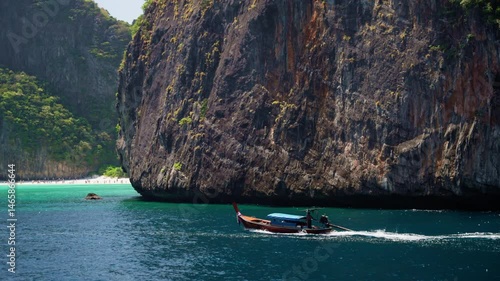 Turquoise waves washing rocky shoreline, longtail boat gliding past maya bay, phi phi leh island, trailing white wake under soft sunlight