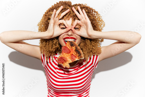 Obraz na płótnie Cheerful woman with curly hair wearing a striped shirt, enjoying a slice of pizza while playfully making funny gestures with her hands, perfect for food and fun concepts w salonie