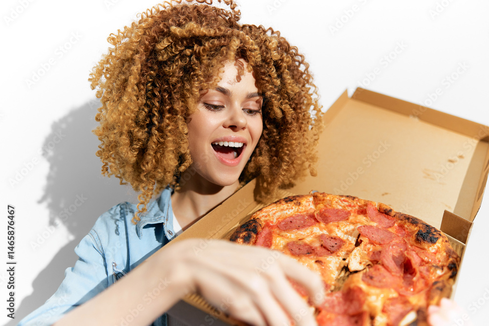 Happy young woman with curly hair enjoying a delicious pizza from a takeaway box, showcasing excitement and joy in a vibrant setting