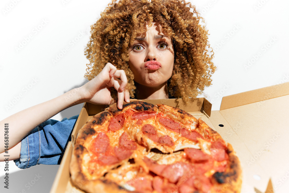 Young woman with curly hair making a funny face while holding a large pizza, expressing humor and joy, perfect for food related concepts