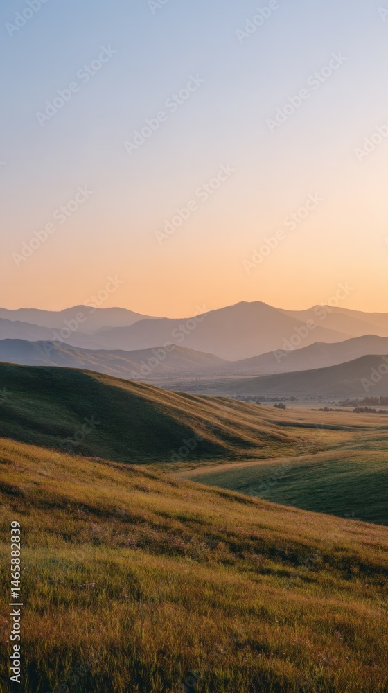 Fototapeta premium Rolling Green Grass Hills and Mountain Range at Soft Sunset Light Vertical View