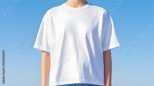 A woman models a plain white, short-sleeved, oversized t-shirt against a bright blue sky.  The shirt is boxy and falls loosely