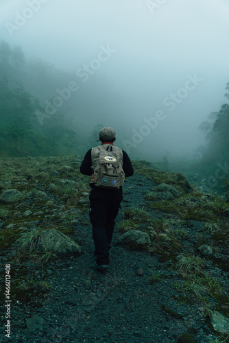 Solo adventurer Walking through a dark and foggy forest while carrying a backpack. An adult Asian male adventurer walks alone in a rocky hill area alone in the thick fog.