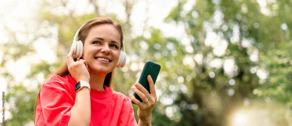 Obraz premium Smiling woman enjoying music with wireless headphones and smartphone outdoors
