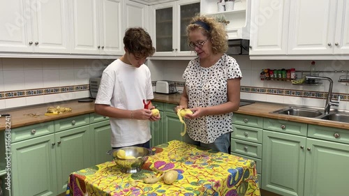 Middle-aged woman and teenage son peeling potatoes together in kitchen preparing traditional Spanish omelette