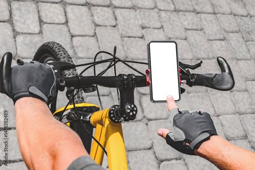 Close-up of a finger in front of a smartphone mockup on a bicycle handlebar. Background of gray paving slabs outdoors.