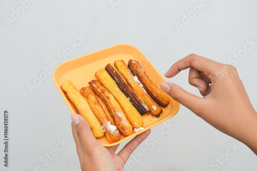 closeup of curos on a yellow plate held by a woman's hand against a white background, is a food made from fried pastry dough, usually choux pastry.
