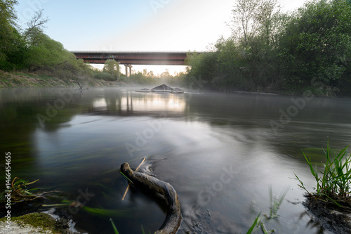 Sunrise over a misty river surrounded by lush green trees in spring. Tranquil nature landscape with calm water, fog, and golden sunlight reflecting on the surface. Ideal for eco, travel, wellness. 