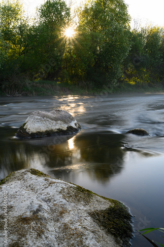 Obraz na płótnie Sunrise over a misty river surrounded by lush green trees in spring. Tranquil nature landscape with calm water, fog, and golden sunlight reflecting on the surface. Ideal for eco, travel, wellness. w salonie