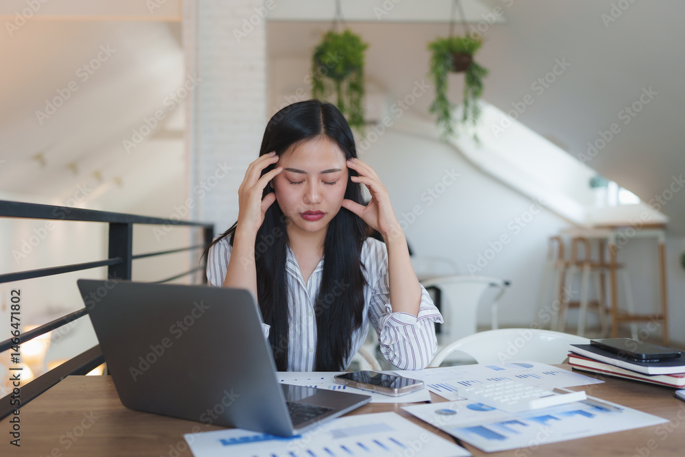 Obraz premium Stressed asian businesswoman having headache while working with laptop in office
