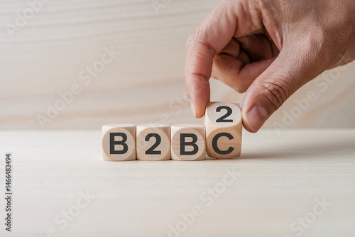 Wooden cubes spelling B2B on light wood table, hand placing last cube, showcasing business-to-business concept
