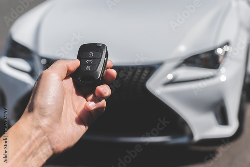 Close-up of a woman unlocking a car using a key fob, with a white car parked in a car park in the background.