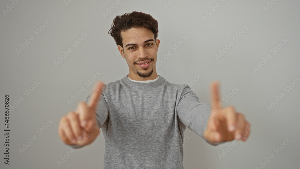 Fototapeta premium Young man with extended fingers smiling confidently against plain white background, embodying a friendly and approachable demeanor