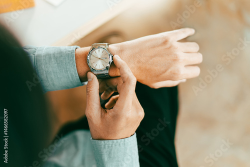 businessman in casual fashion checks his stainless wristwatch is waiting for his next appointment focused on time cooperation and consulting, topview above.