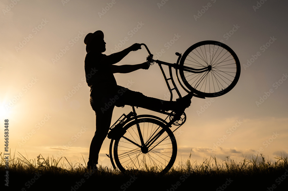Obraz premium The silhouette of a cyclist stands on the back wheel of a bicycle or bike. Sunset background.