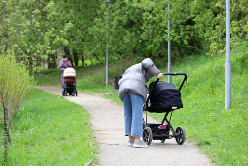 Obraz na płótnie Mothers walking with baby prams in city park at spring. Woman with stroller in foreground w salonie