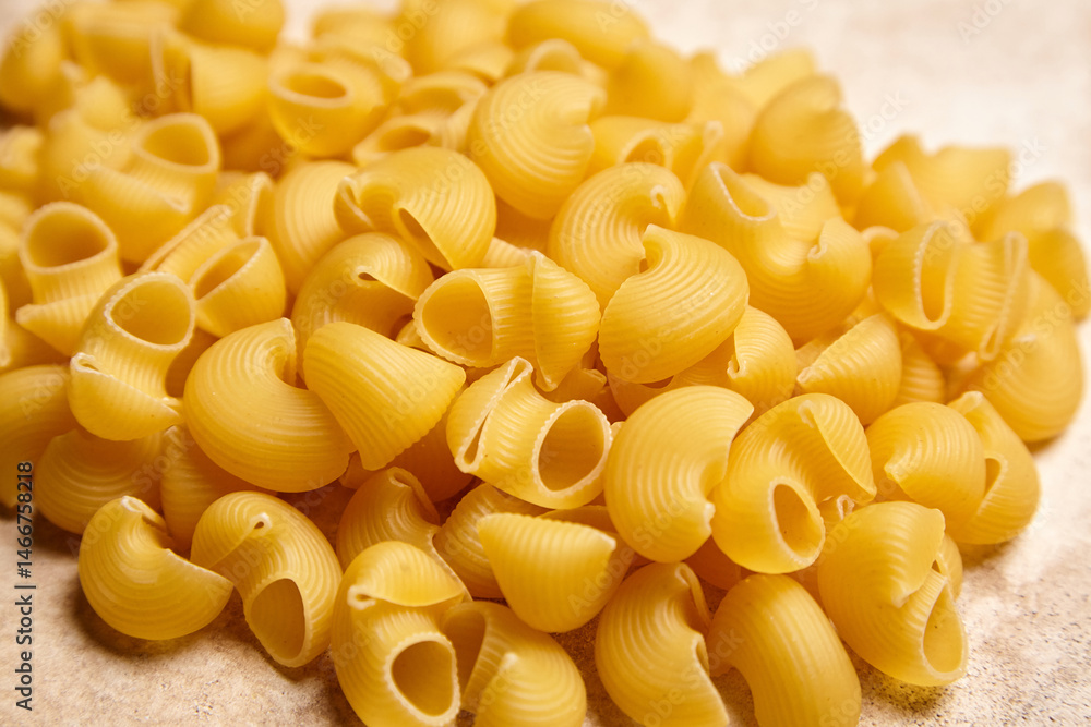 Close-up of uncooked pipe rigate pasta with ribbed, hollow shapes scattered on a light neutral surface, ideal for food packaging and recipe visuals Close-up of uncooked pipe rigate pasta with ribbed, hollow shapes scattered on a light neutral surface, ideal for food packaging and recipe visuals