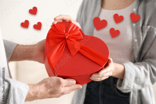 Lovely couple with gift box indoors, closeup. Drawn hearts near them