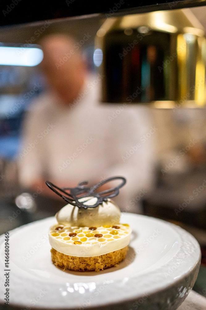 Gourmet dessert with honeycomb-patterned cream, chocolate decoration, and whipped cream, elegantly plated in a professional kitchen.