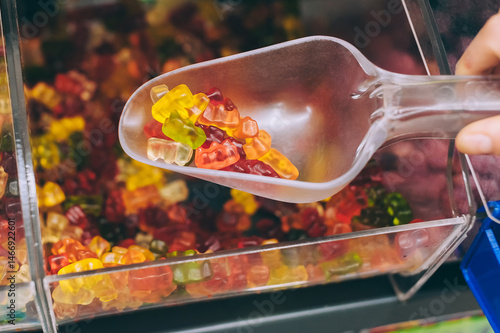 Hand with scoop taking colorful gummy bears in candy store.