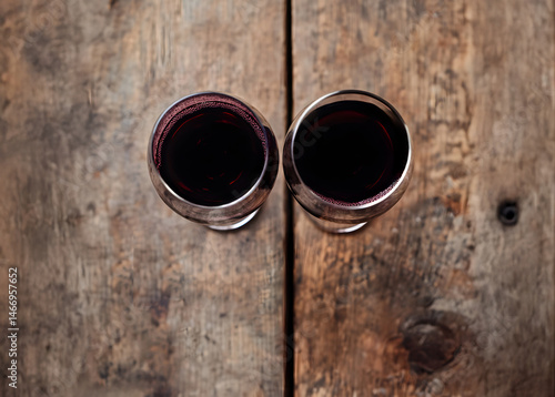 Obraz na płótnie Top-down composition showing two red wine glasses on rustic wooden table, highlighting rich reflections and textures under soft lighting in indoor setting ideal for gourmet or lifestyle visuals. w salonie