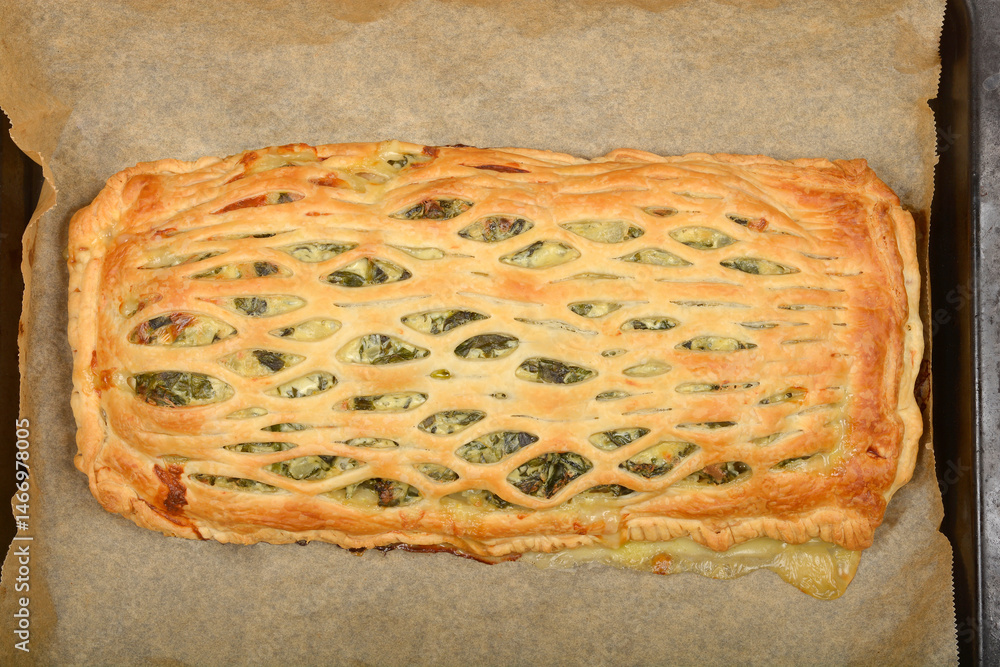 An overhead shot shows a baked puff pastry pie filled with spinach and cheese on parchment paper