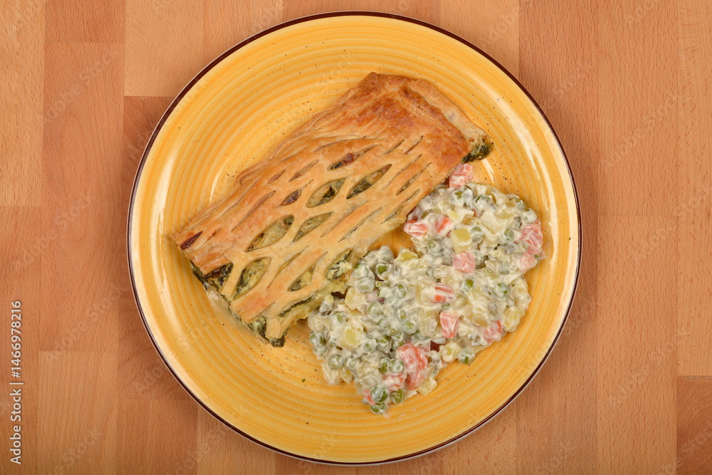 A top-down view shows a slice of spinach and cheese puff pastry served with Croatian-style French salad on an yellow plate