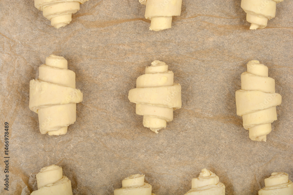 An overhead close-up of raw, rolled croissant dough pieces arranged on parchment paper before baking